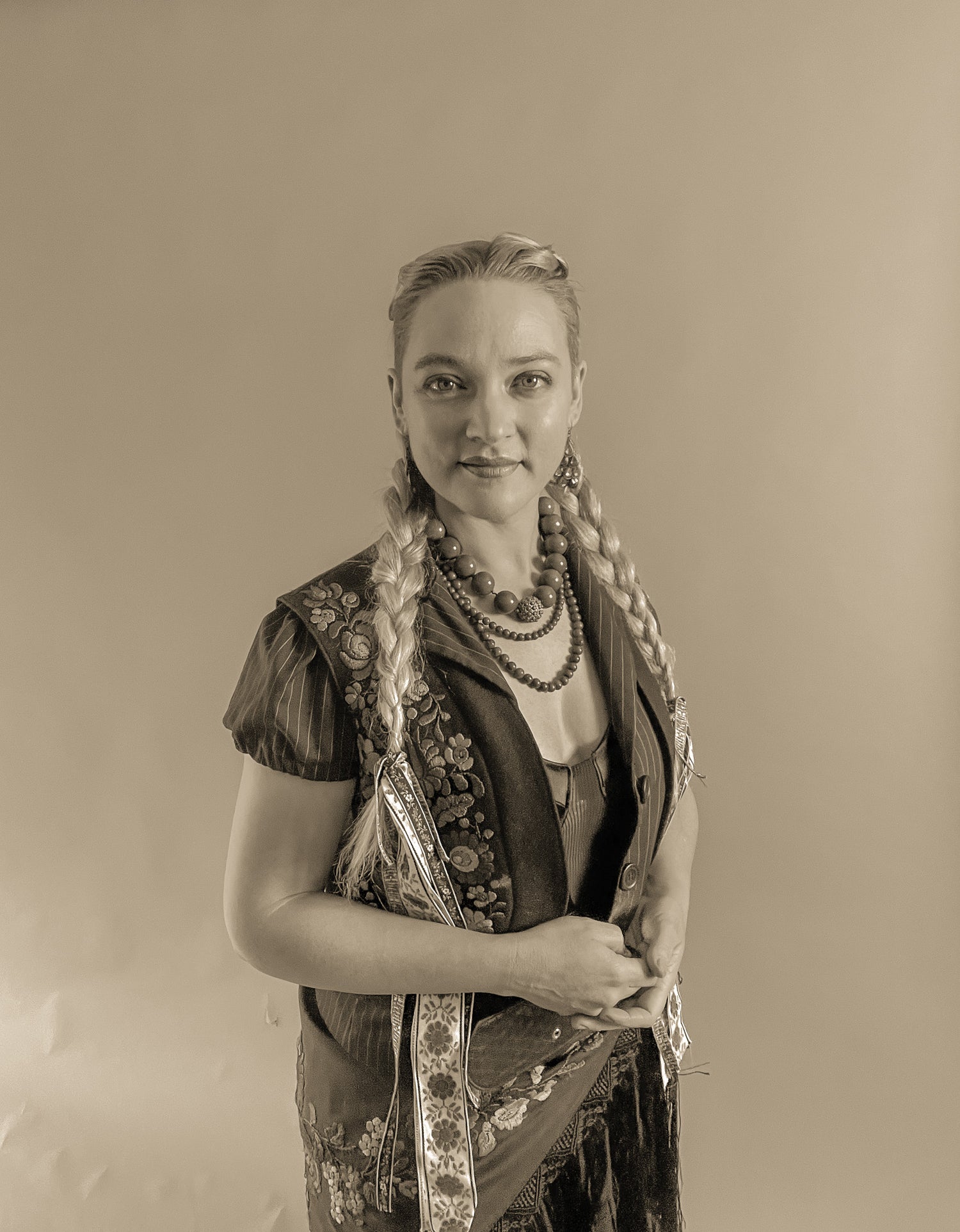 Krisztianna stands in her studio in a sepia tone image, wearing her Hungarian Folk attire and hair style